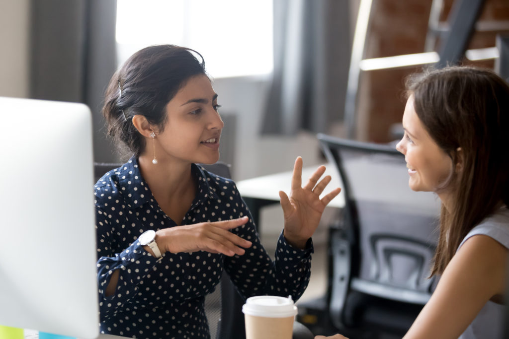 Two women talking at an office desk about how to improve sales