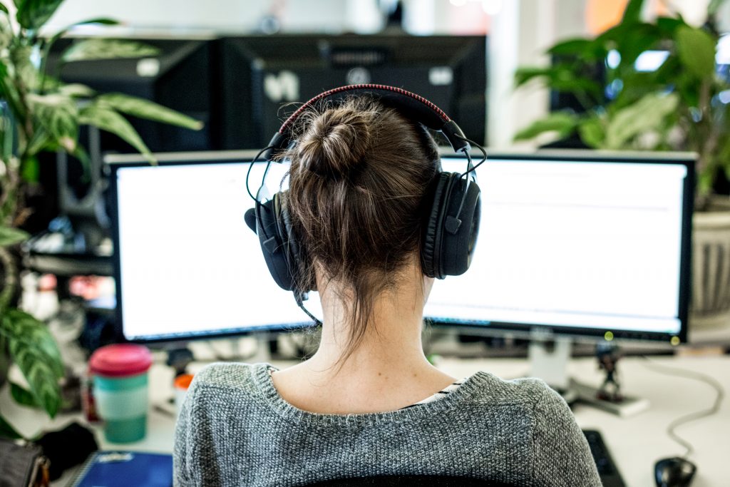 Employee wearing headphones and sitting at a desk with two display screens